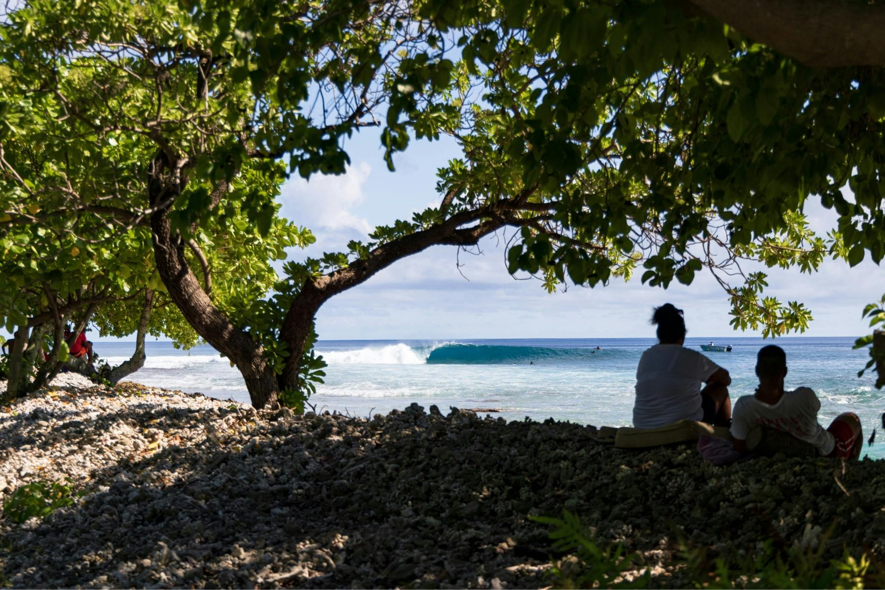 Two men sit on a beach while watching the surf photo by Ryan Chachi Craig