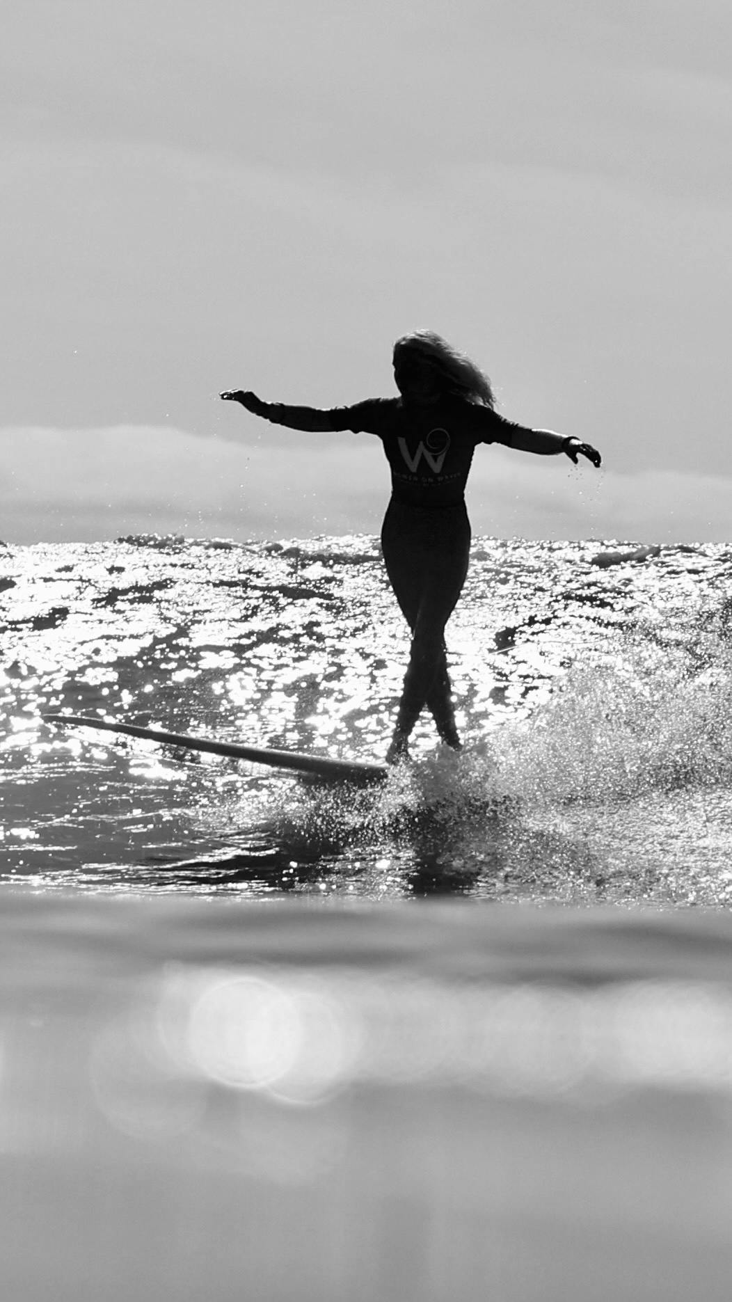 A female surfer rides a wave with both arms stretched outward