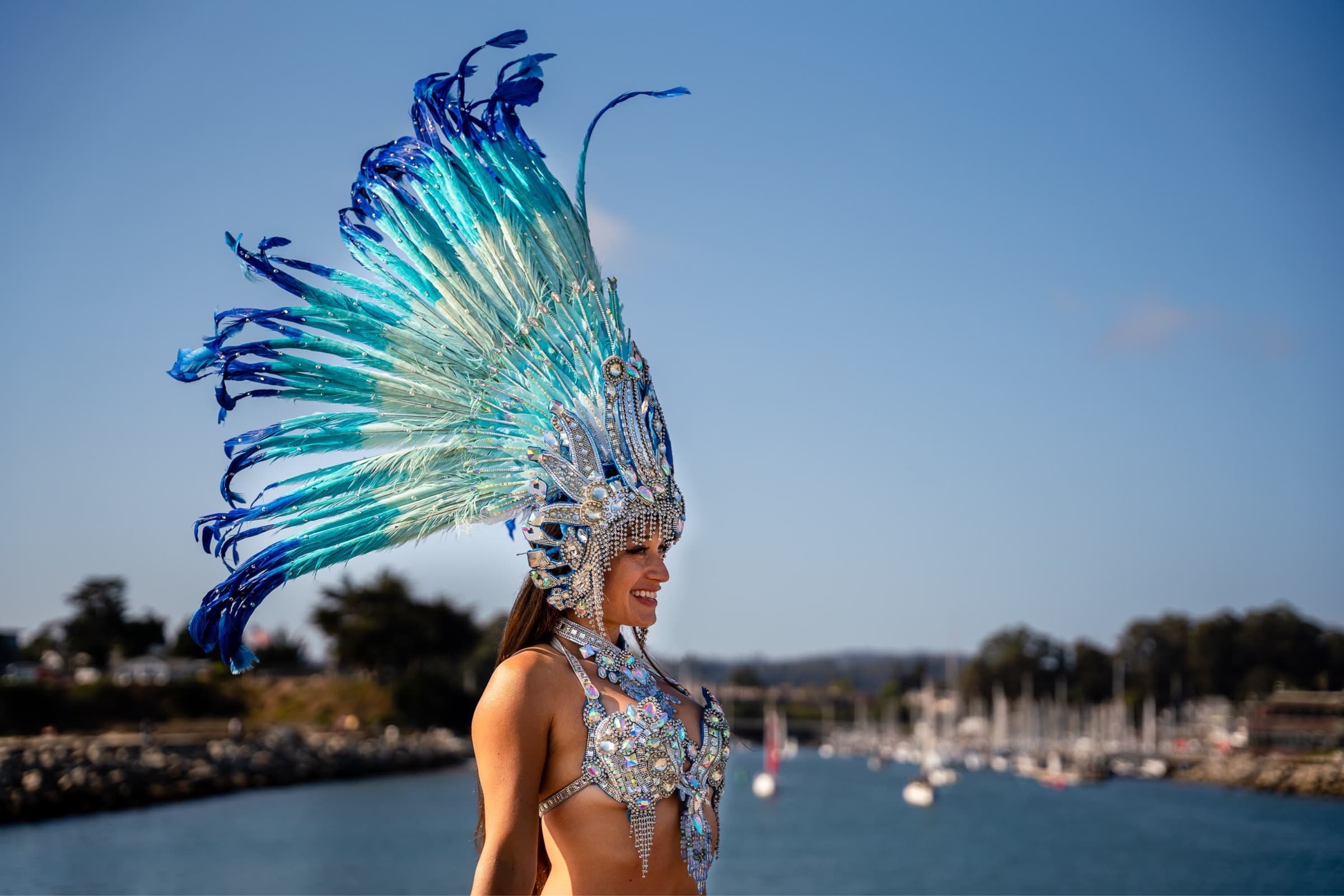 Gisella Ferreira smiles while wearing samba attire with the Santa Cruz harbor in the background