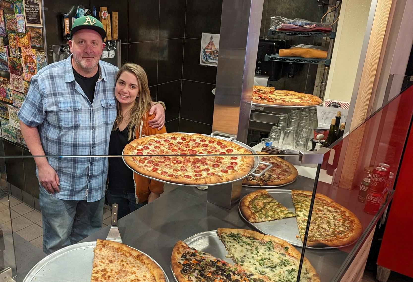 Sol Lipman and his partner Erica stand behind a counter full of pizzas at their Downtown Santa Cruz Pleasure Pizza