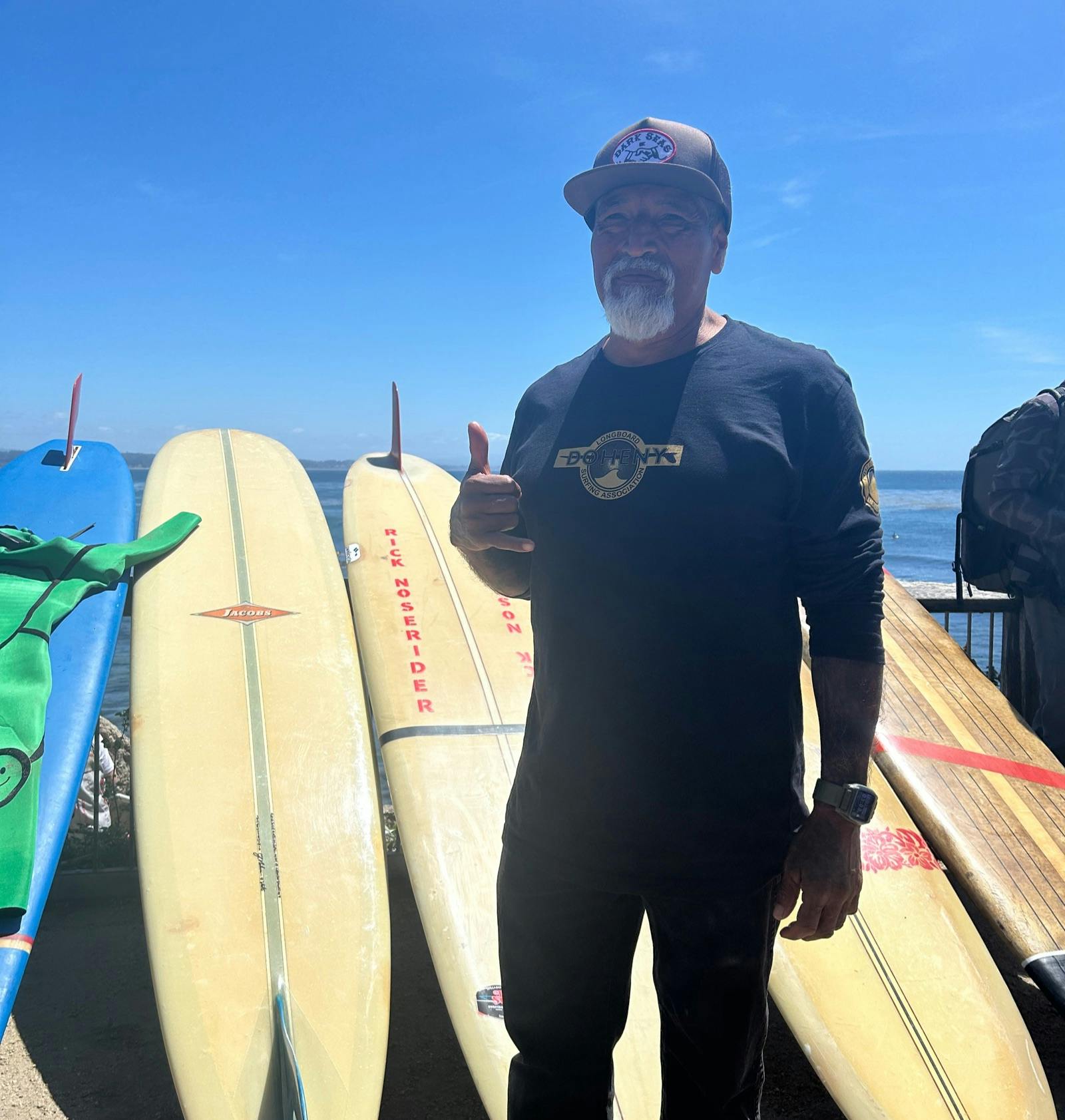 Marciano “Chango” Cruz stands in front of a row of surfboards at Pleasure Point in Santa Cruz, CA