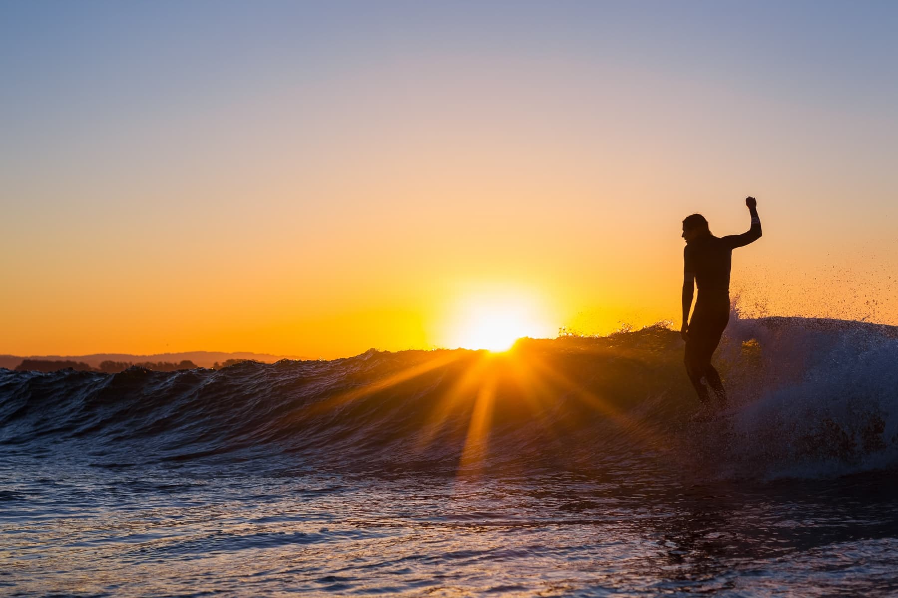 Surfer Darshan Gooch catches a ride while sunlight just barely peaks over the lip of his wave