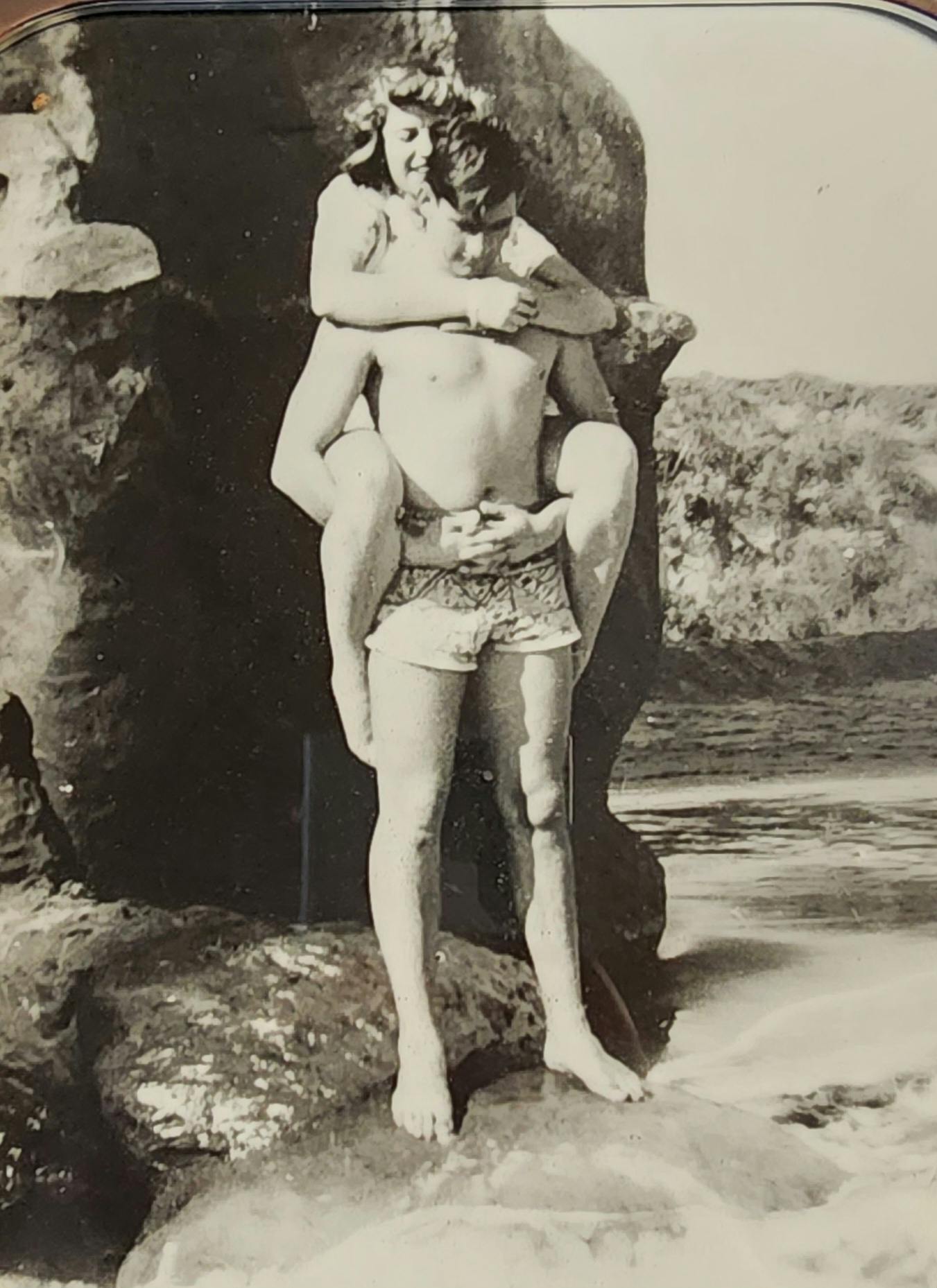 Ritt stands on a rock along the shore while holding a friend on his back