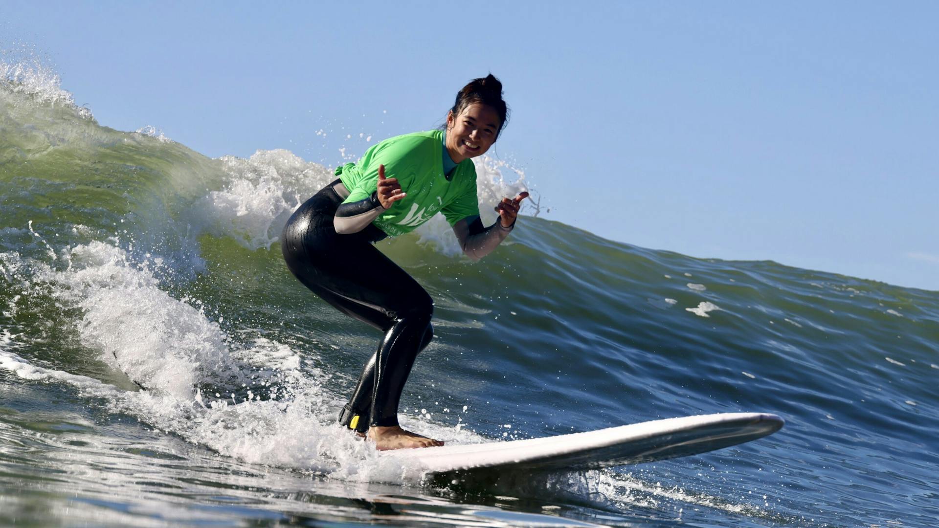 A female surfer rides a wave while display the shaka sign on both hands