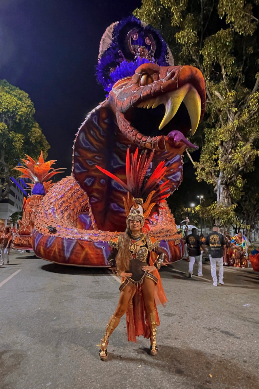 Gisella Ferreira stands in front of a large carnival parade float of a snake while wearing samba attire