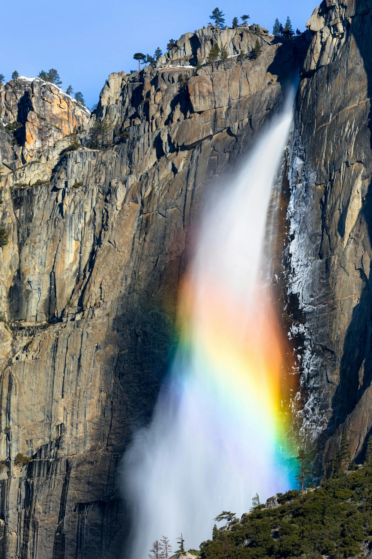 A segment of a rainbow spans across the middle of a flowing waterfall at Yosemite National Park