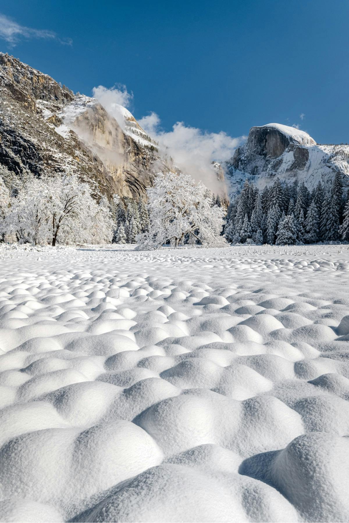 Small mounds of snow cover a wintery landscape with mountains in the background of Yosemite National Park