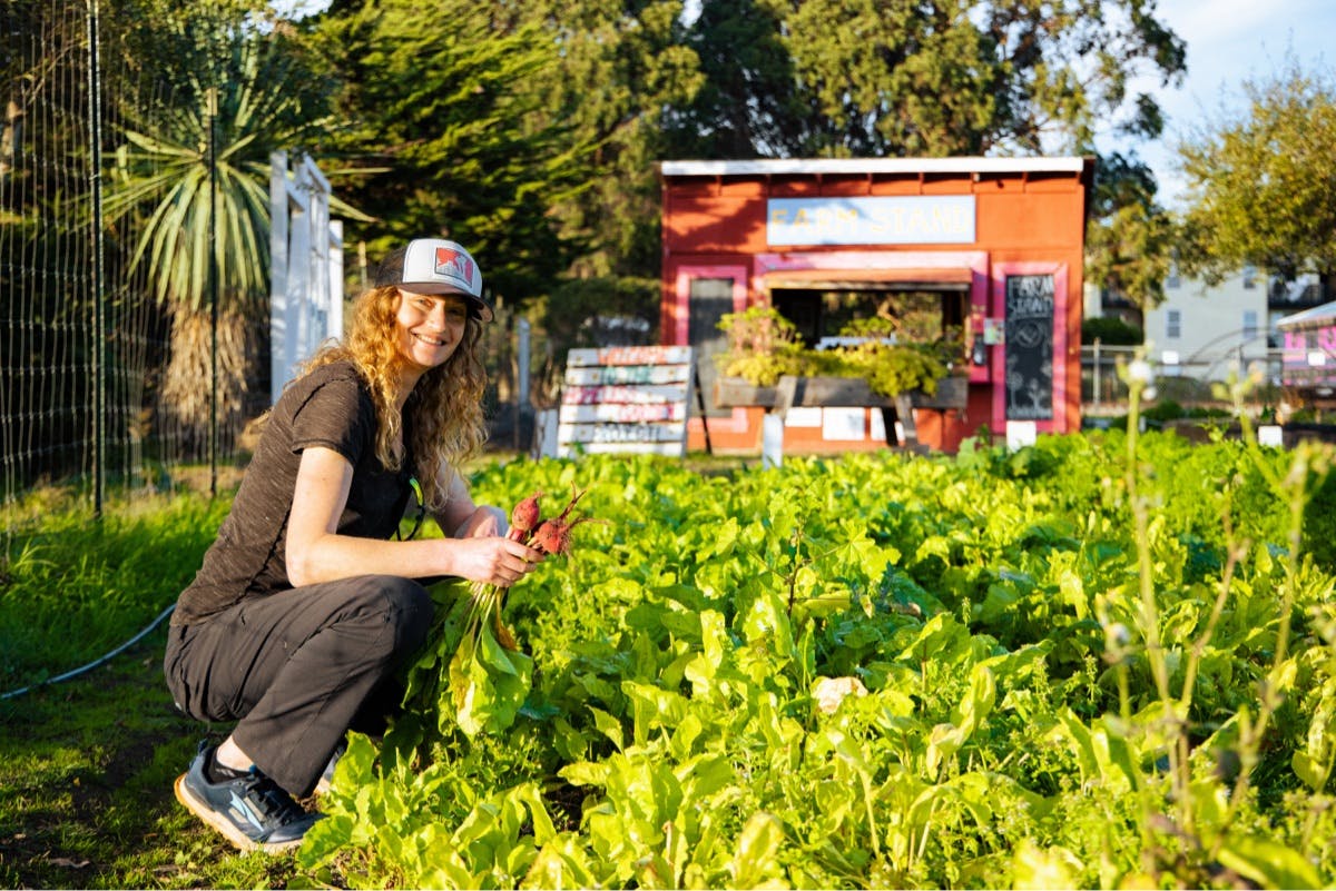 A woman smiles while holding freshly picked beets from the Santa Cruz Homeless Garden Project